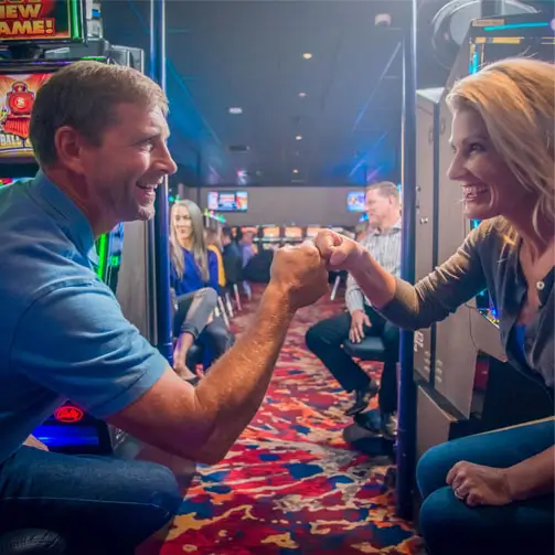 Two guests fist bumping between slot machines.